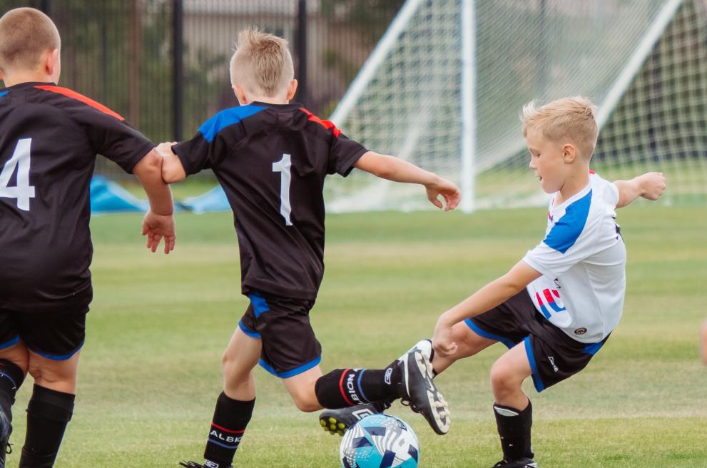 Drie jonge jongens, van twee verschillende ploegen, spelen voetbal.