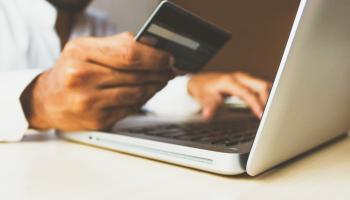 Persoon zit aan laptop en houdt betaalkaart vast om onlinebetaling uit te voeren